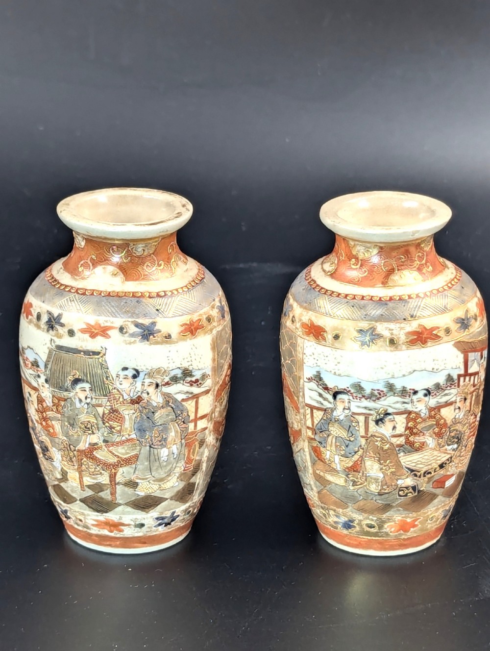 A pair of small Japanese Kutani porcelain vases featuring figurative narrative panels framed by iron-red and gold leaf borders.