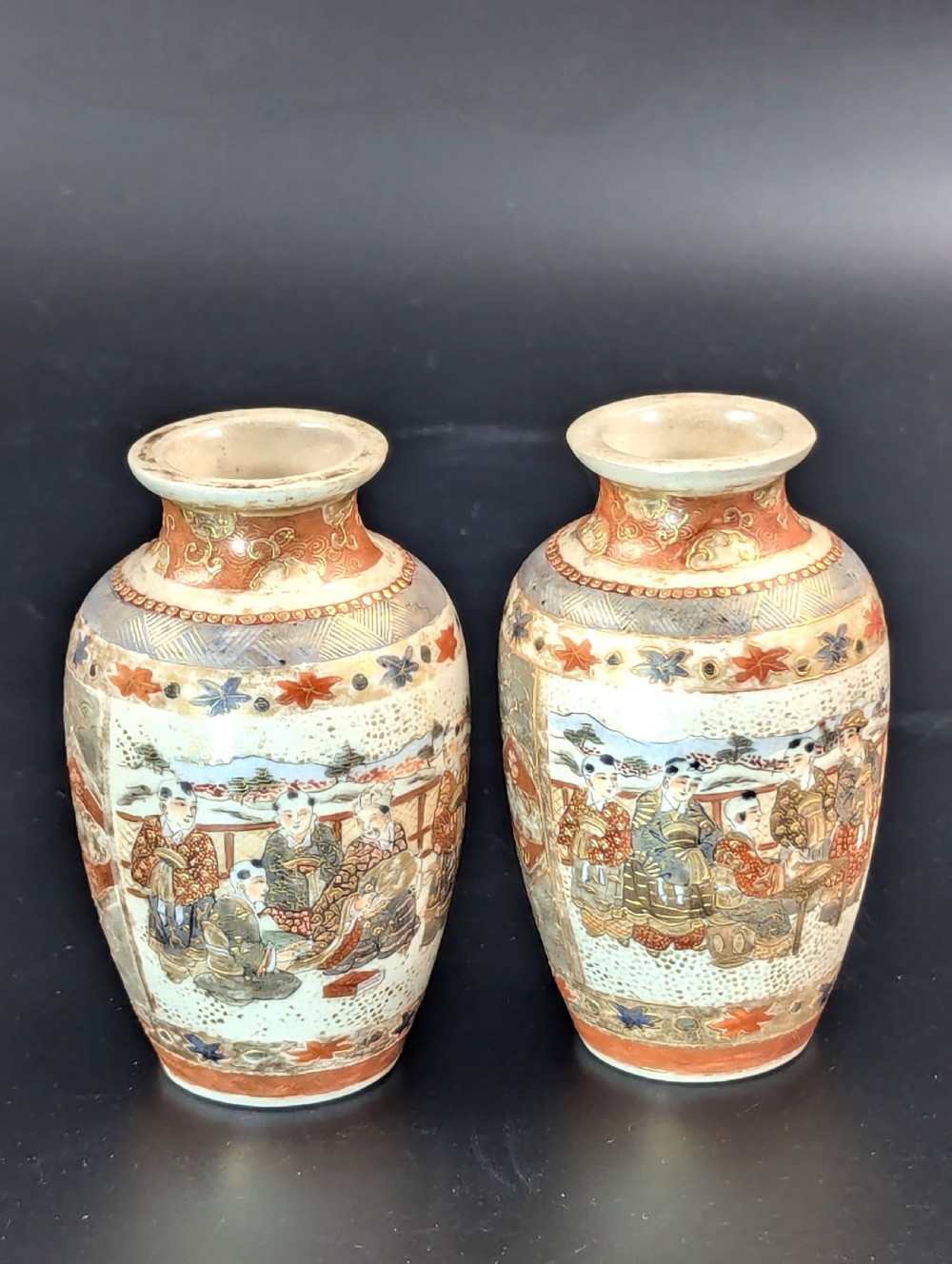 A pair of small Japanese Kutani porcelain vases featuring figurative narrative panels framed by iron-red and gold leaf borders. View III