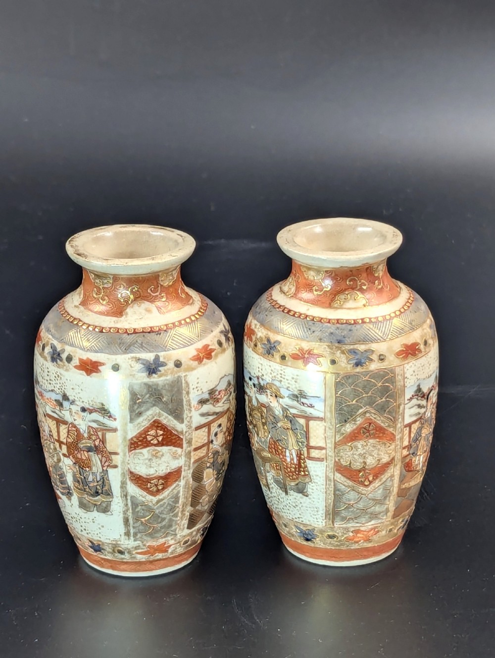 A pair of small Japanese Kutani porcelain vases featuring figurative narrative panels framed by iron-red and gold leaf borders. View IV