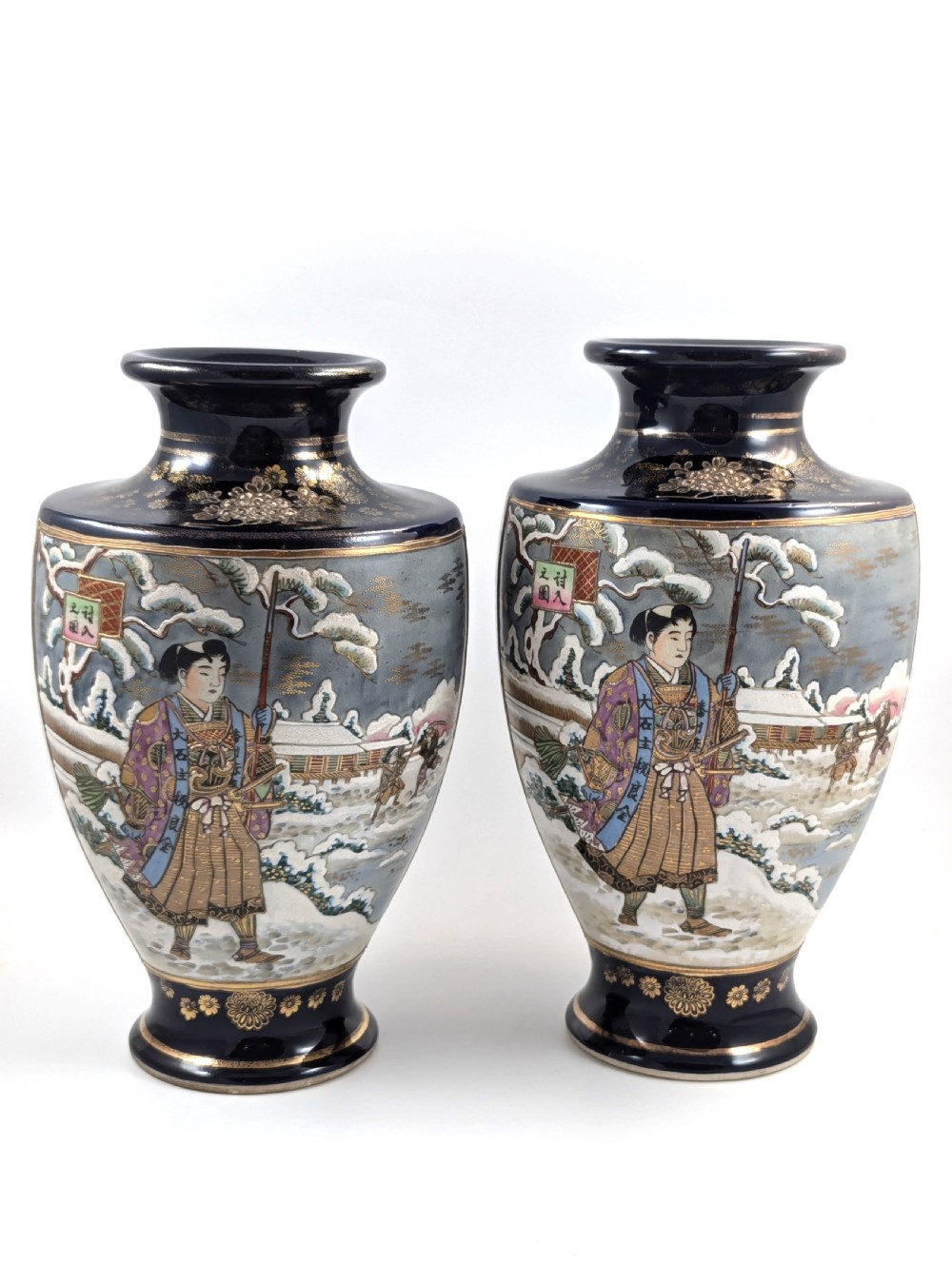A pair of Japanese Satsuma baluster vases featuring painted figures in a snowy landscape framed by cobalt blue and gilded borders.