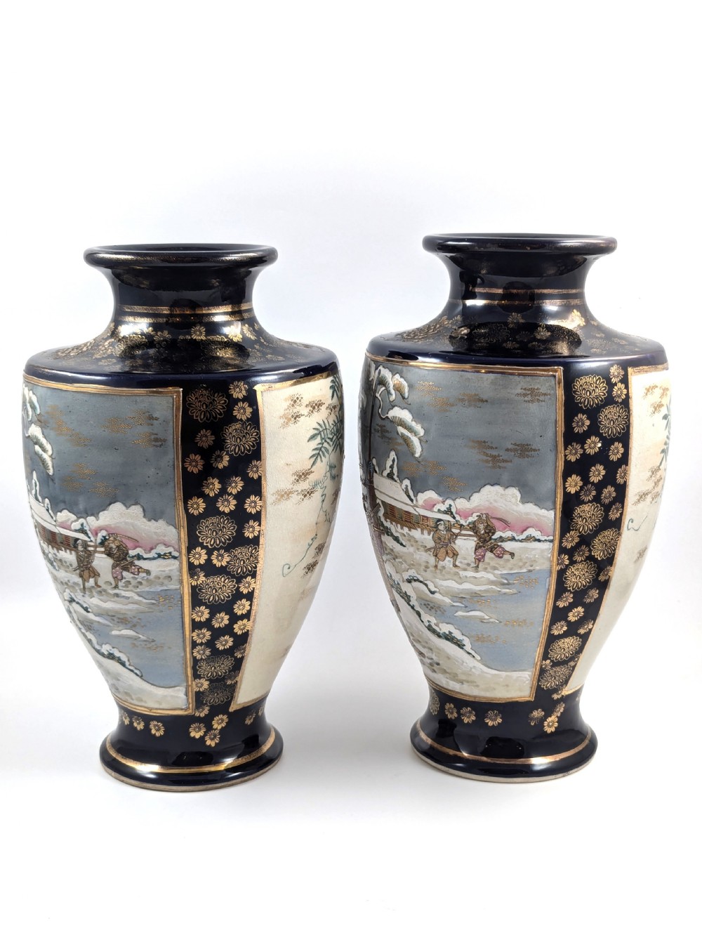 A pair of Japanese Satsuma baluster vases featuring painted figures in a snowy landscape framed by cobalt blue and gilded borders. View II