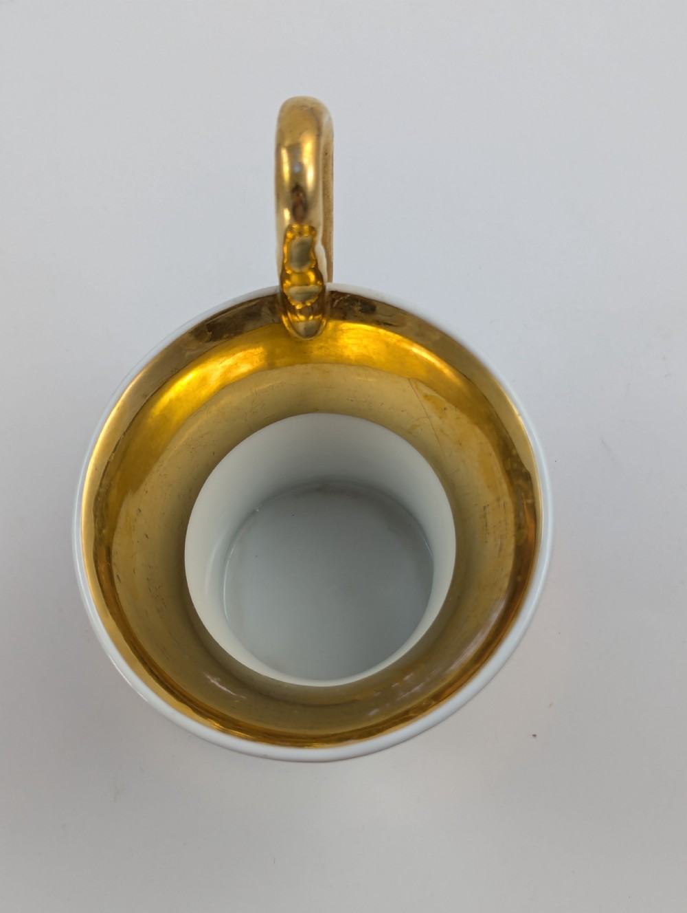 A Neoclassical KPM Berlin porcelain teacup and saucer featuring heavy gold leaf gilding, a maroon background with star patterns, and a high curved loop handle. View VIII