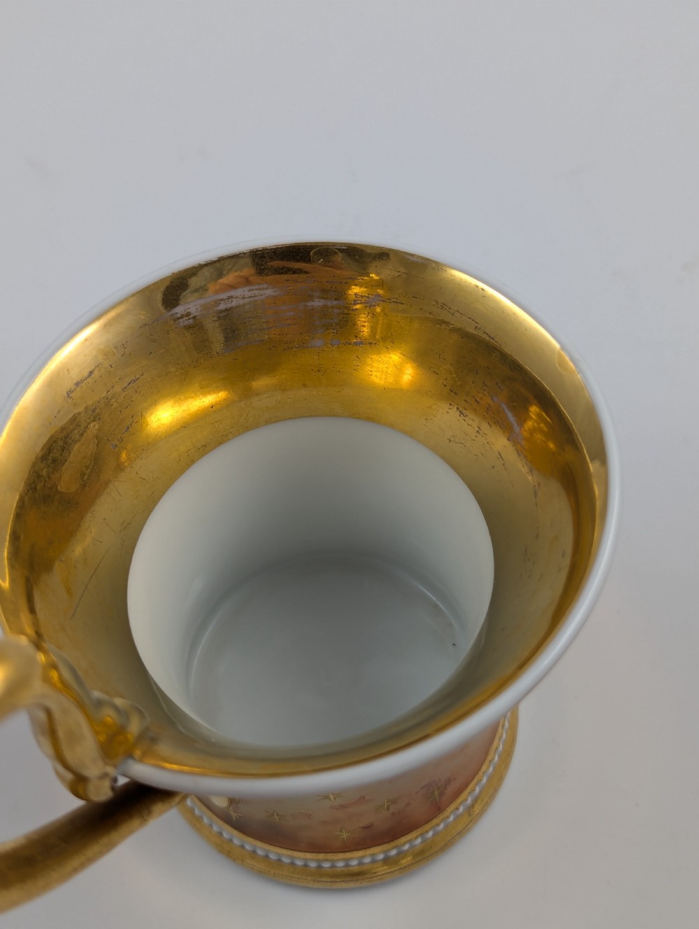 A Neoclassical KPM Berlin porcelain teacup and saucer featuring heavy gold leaf gilding, a maroon background with star patterns, and a high curved loop handle. View XII
