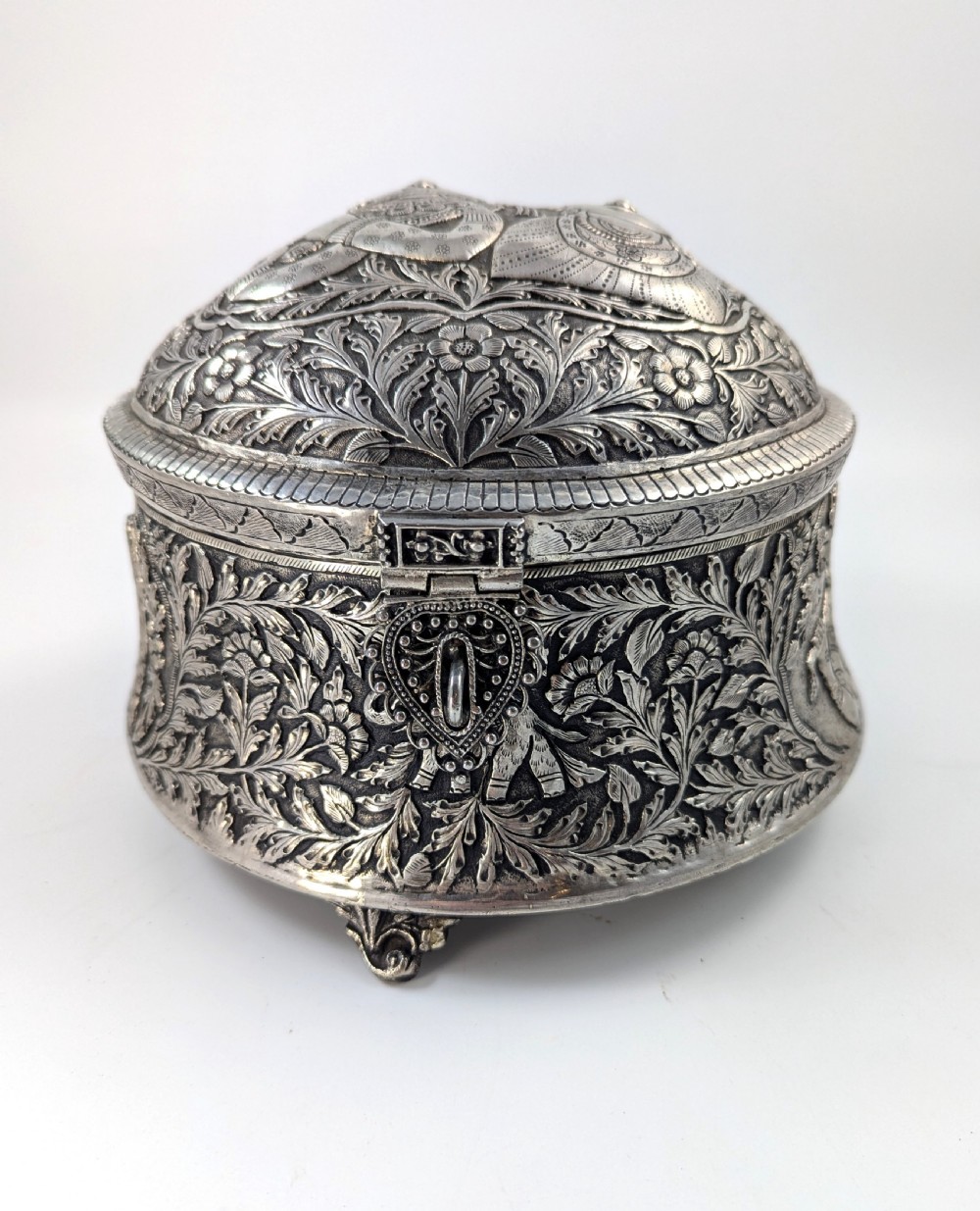 A circular silver-plated box decorated with intricate chased floral motifs and low-relief figures of Krishna and Radha on the lid. View III