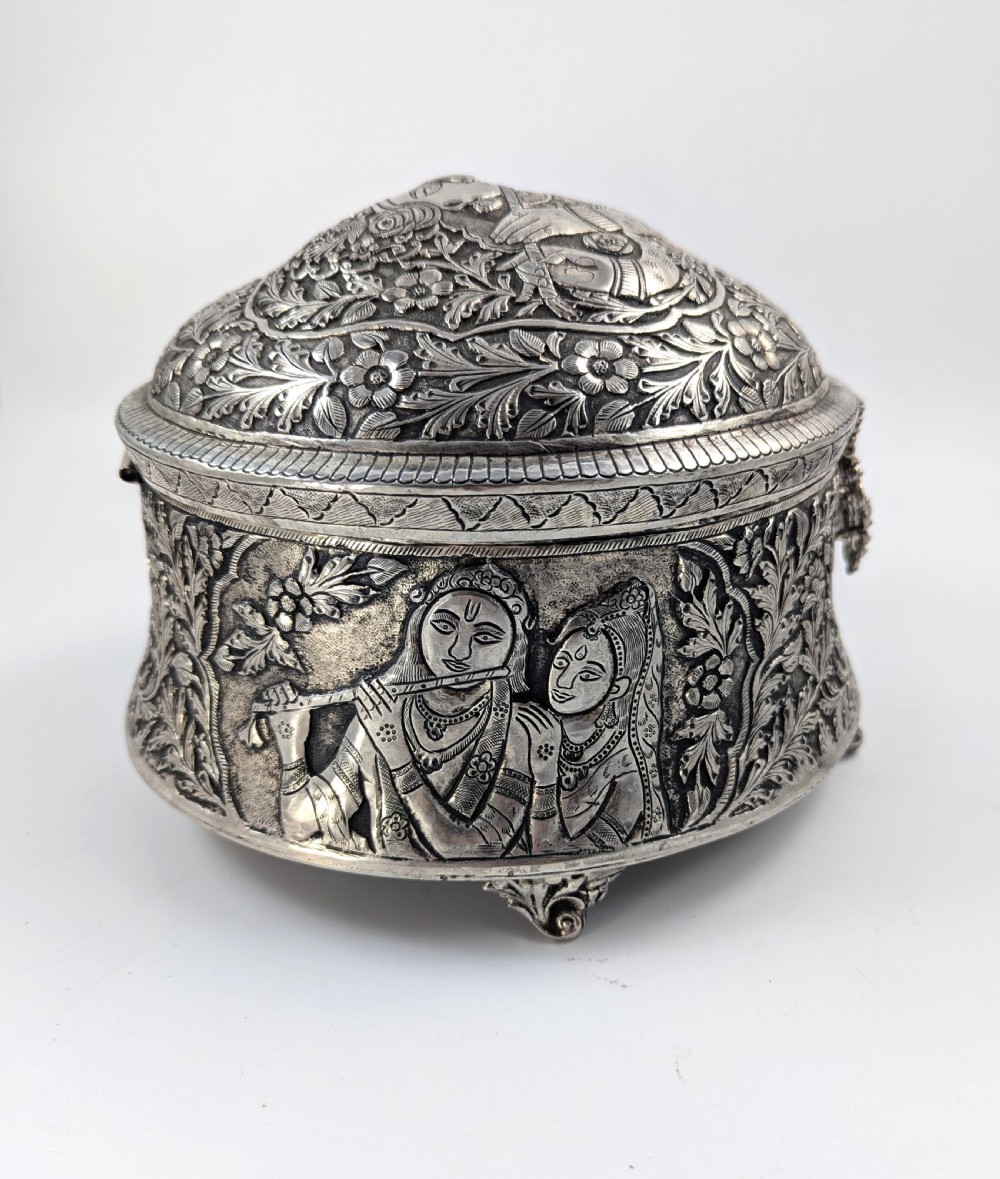 A circular silver-plated box decorated with intricate chased floral motifs and low-relief figures of Krishna and Radha on the lid. View IV