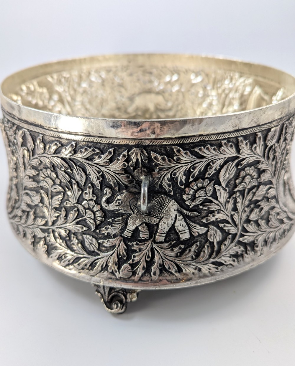 A circular silver-plated box decorated with intricate chased floral motifs and low-relief figures of Krishna and Radha on the lid. View V