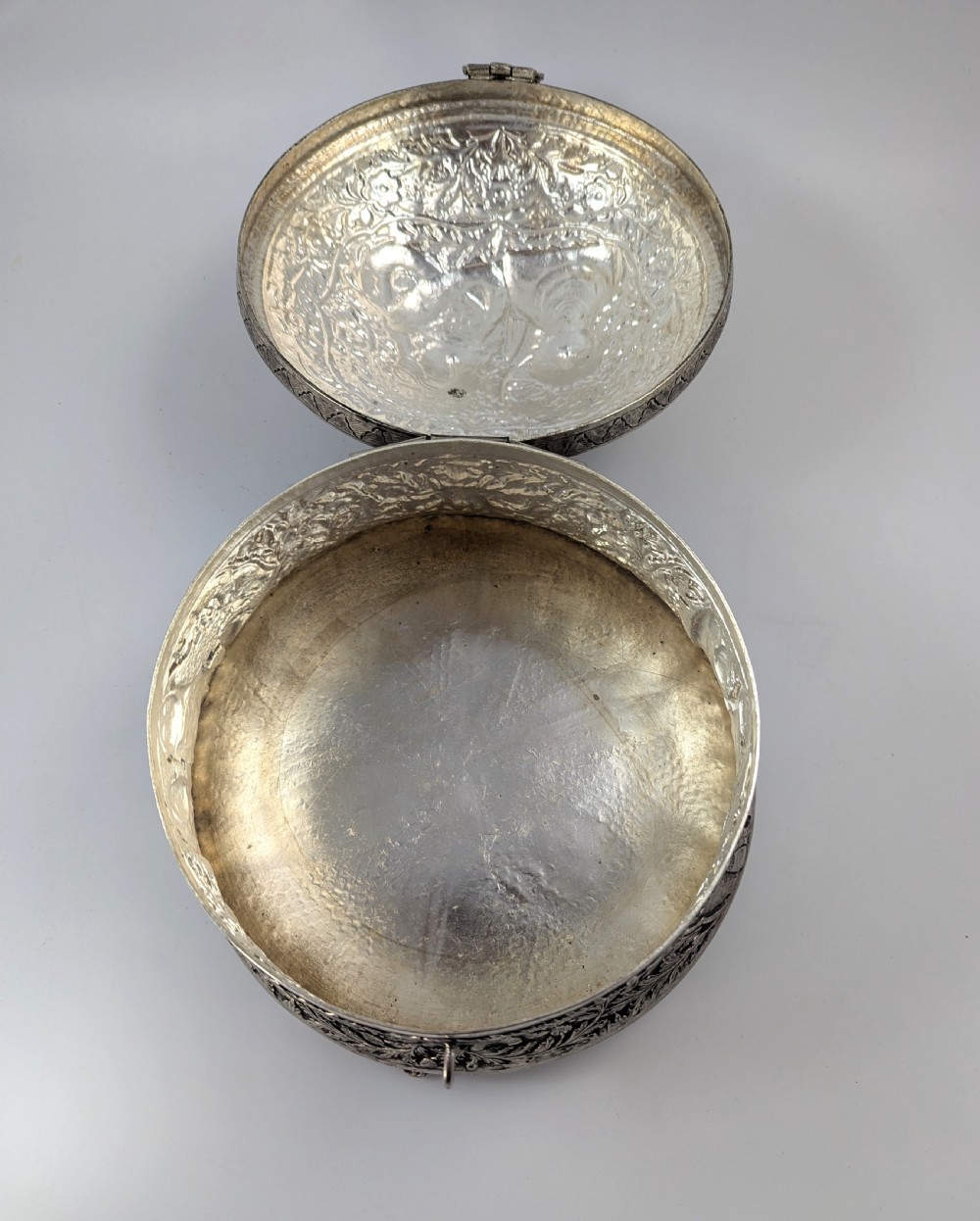 A circular silver-plated box decorated with intricate chased floral motifs and low-relief figures of Krishna and Radha on the lid. View VI