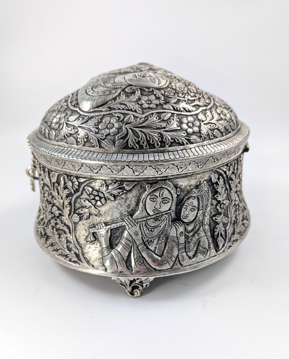 A circular silver-plated box decorated with intricate chased floral motifs and low-relief figures of Krishna and Radha on the lid. View VIII