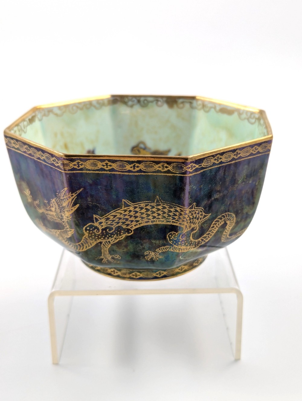 An octagonal blue iridescent porcelain bowl featuring gilded dragon motifs and geometric gold trim around the rim.