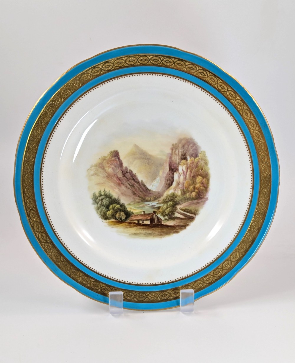 A circular Victorian porcelain cabinet plate featuring a hand-painted landscape scene encircled by a turquoise border with gilded tooling.