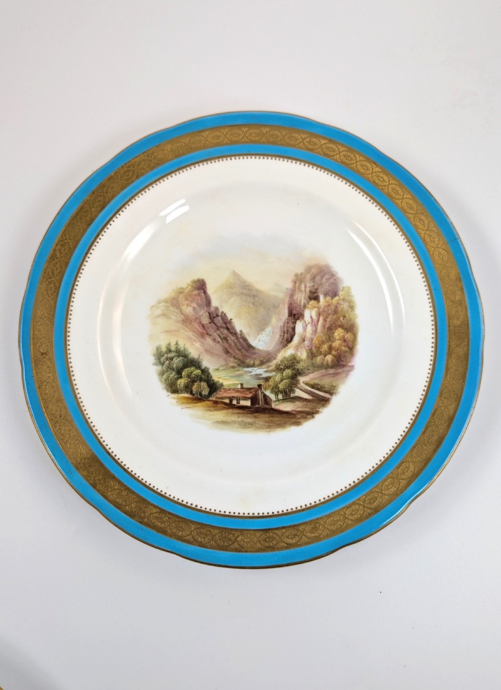 A circular Victorian porcelain cabinet plate featuring a hand-painted landscape scene encircled by a turquoise border with gilded tooling. View VI