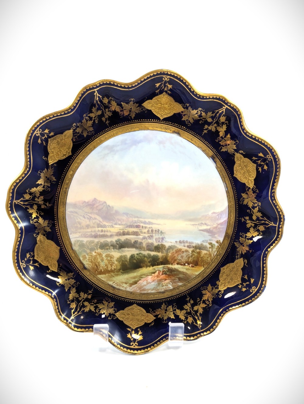A Victorian Aynsley porcelain cabinet plate featuring a central hand-painted landscape surrounded by a scalloped cobalt blue border with intricate gold leaf ornamentation. View II