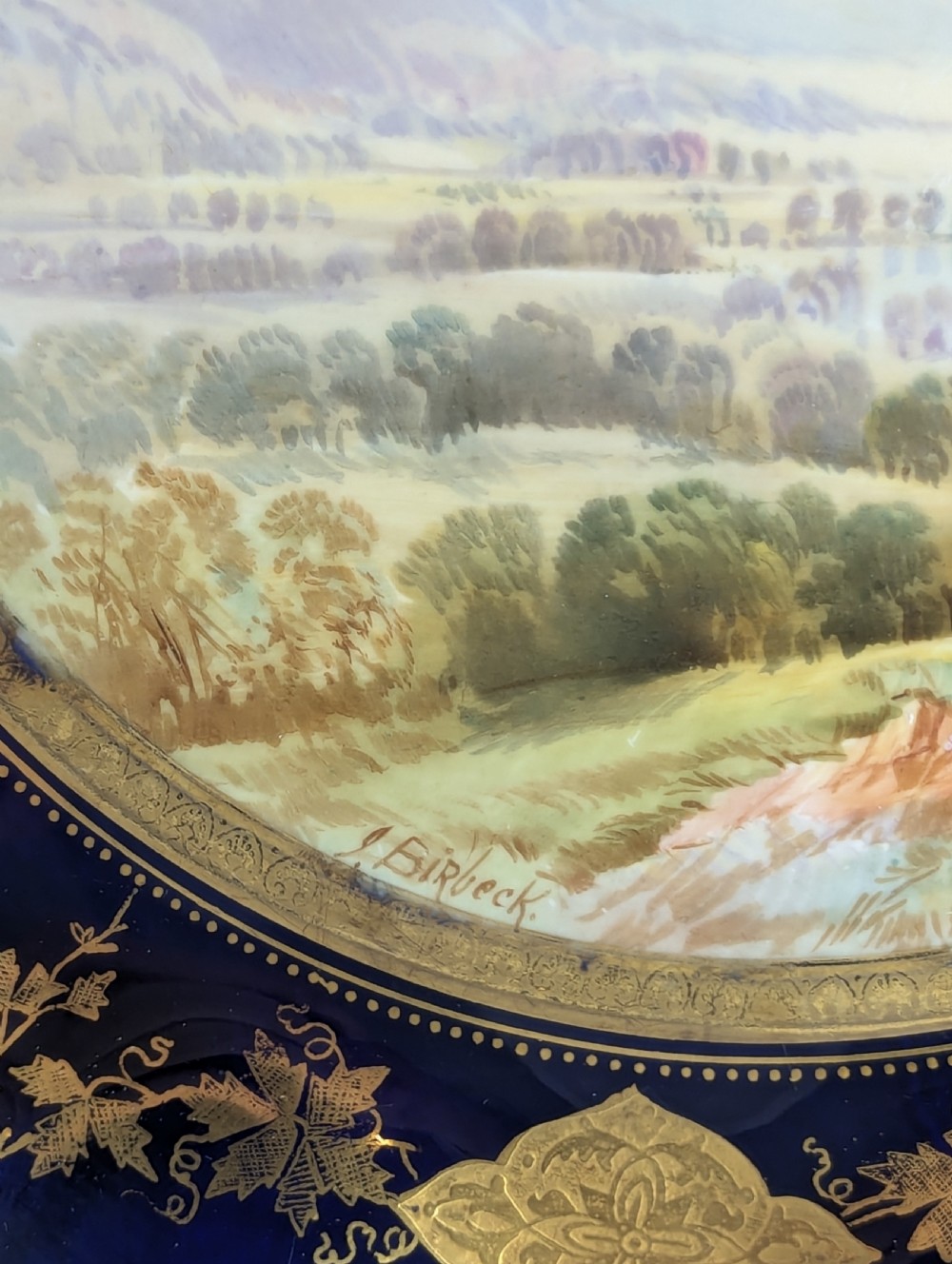 A Victorian Aynsley porcelain cabinet plate featuring a central hand-painted landscape surrounded by a scalloped cobalt blue border with intricate gold leaf ornamentation. View IV