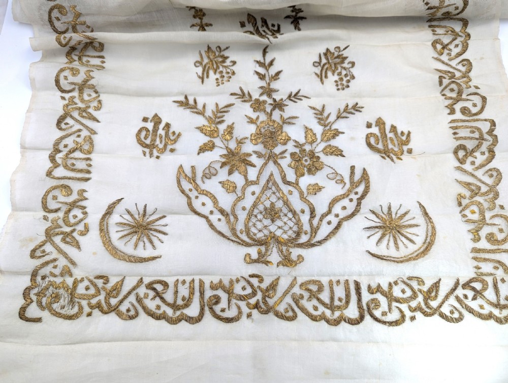 A light cream silk scarf featuring metallic gold thread hand embroidery with floral motifs, crescent symbols, and calligraphic borders.