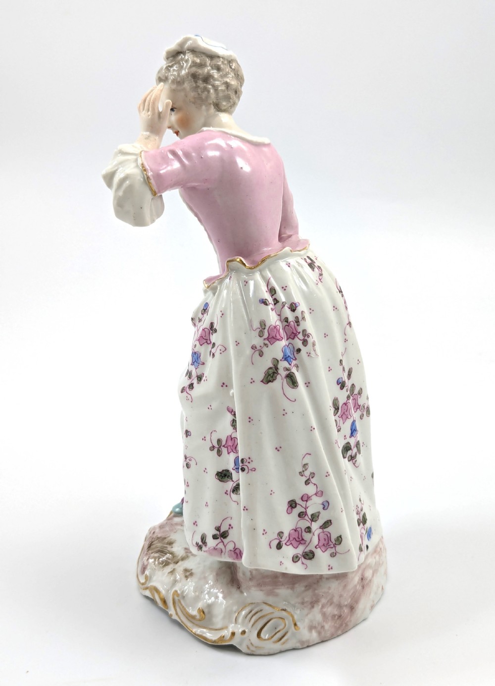 An antique French Samson porcelain figurine depicting a woman in eighteenth-century attire with a pink bodice and floral skirt standing on a scrollwork base. View III
