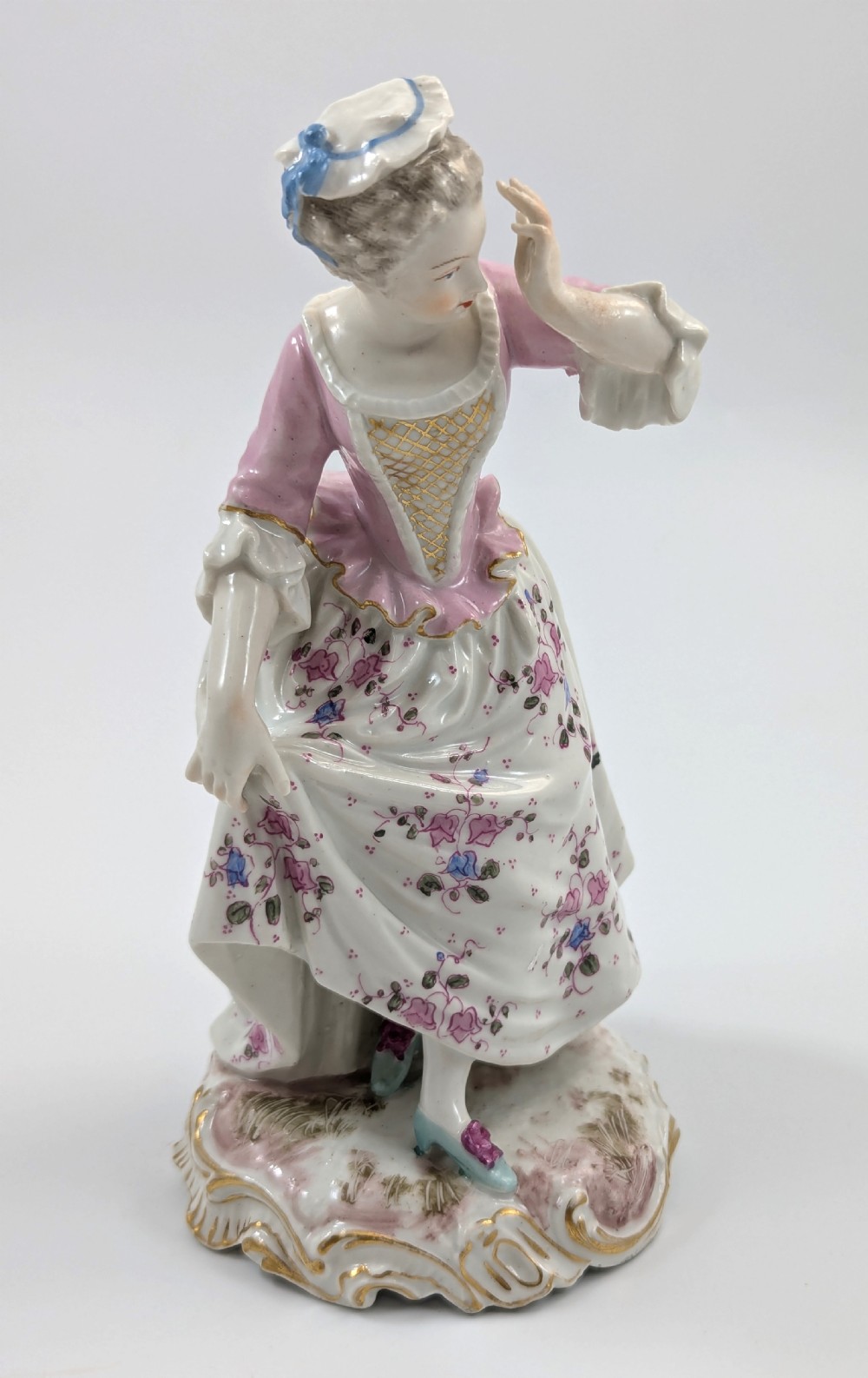 An antique French Samson porcelain figurine depicting a woman in eighteenth-century attire with a pink bodice and floral skirt standing on a scrollwork base. View V
