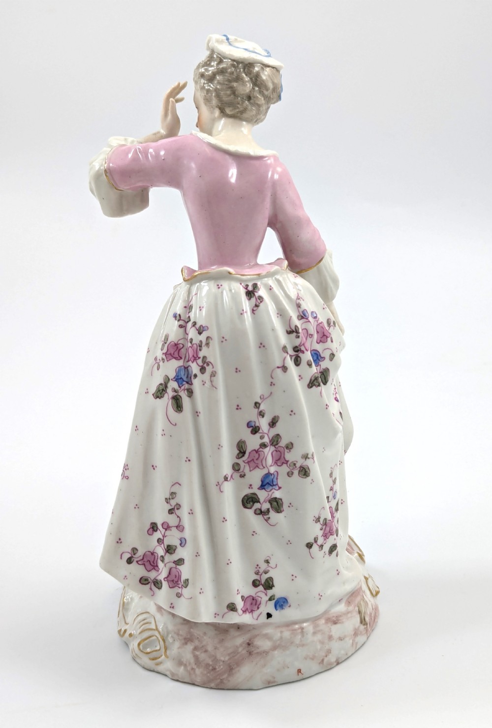 An antique French Samson porcelain figurine depicting a woman in eighteenth-century attire with a pink bodice and floral skirt standing on a scrollwork base. View VI