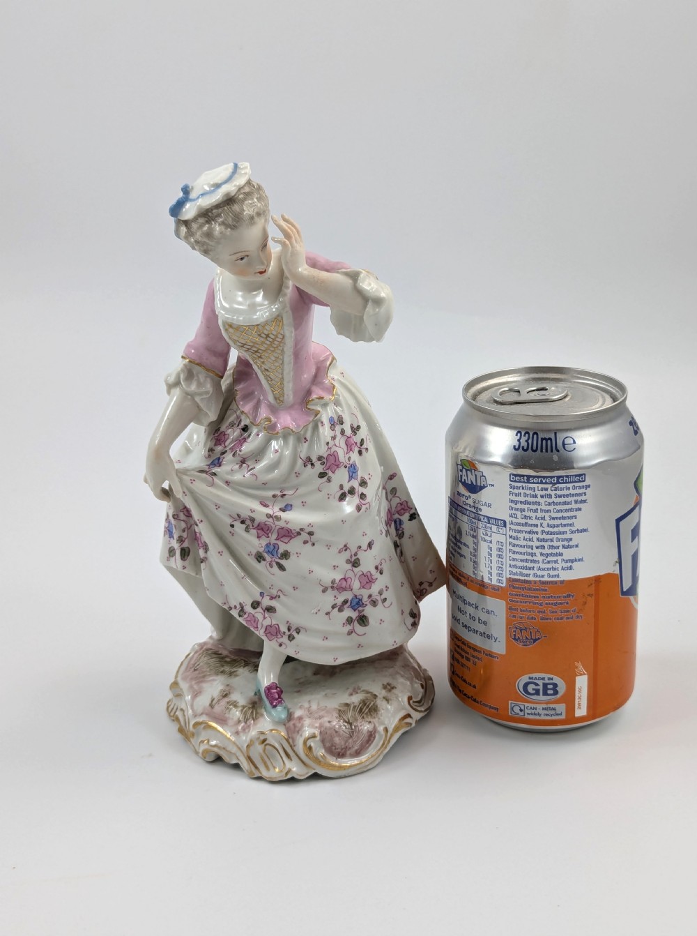 An antique French Samson porcelain figurine depicting a woman in eighteenth-century attire with a pink bodice and floral skirt standing on a scrollwork base. View VIII