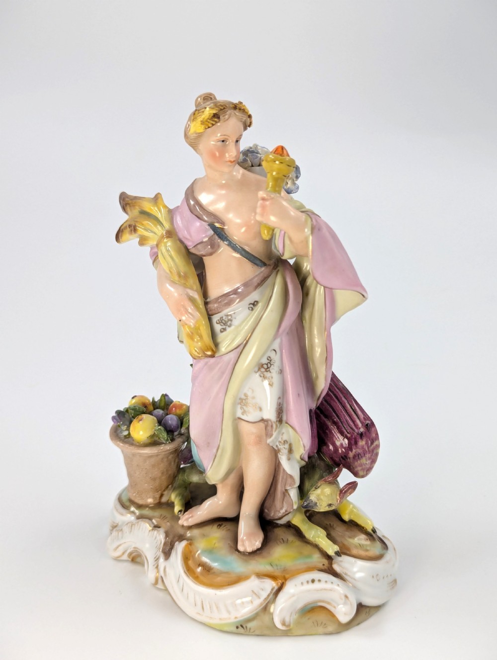 Late 19th-century German Volkstedt porcelain allegorical figurine depicting a draped female figure holding a torch and sheaf of wheat atop a gilded scroll base.