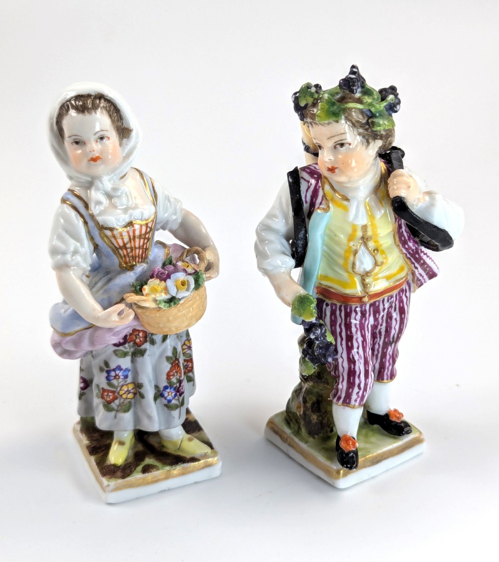 Pair of late 19th-century Helena Wolfsohn porcelain child figurines featuring hand-painted floral attire, baskets, and gilded bases.