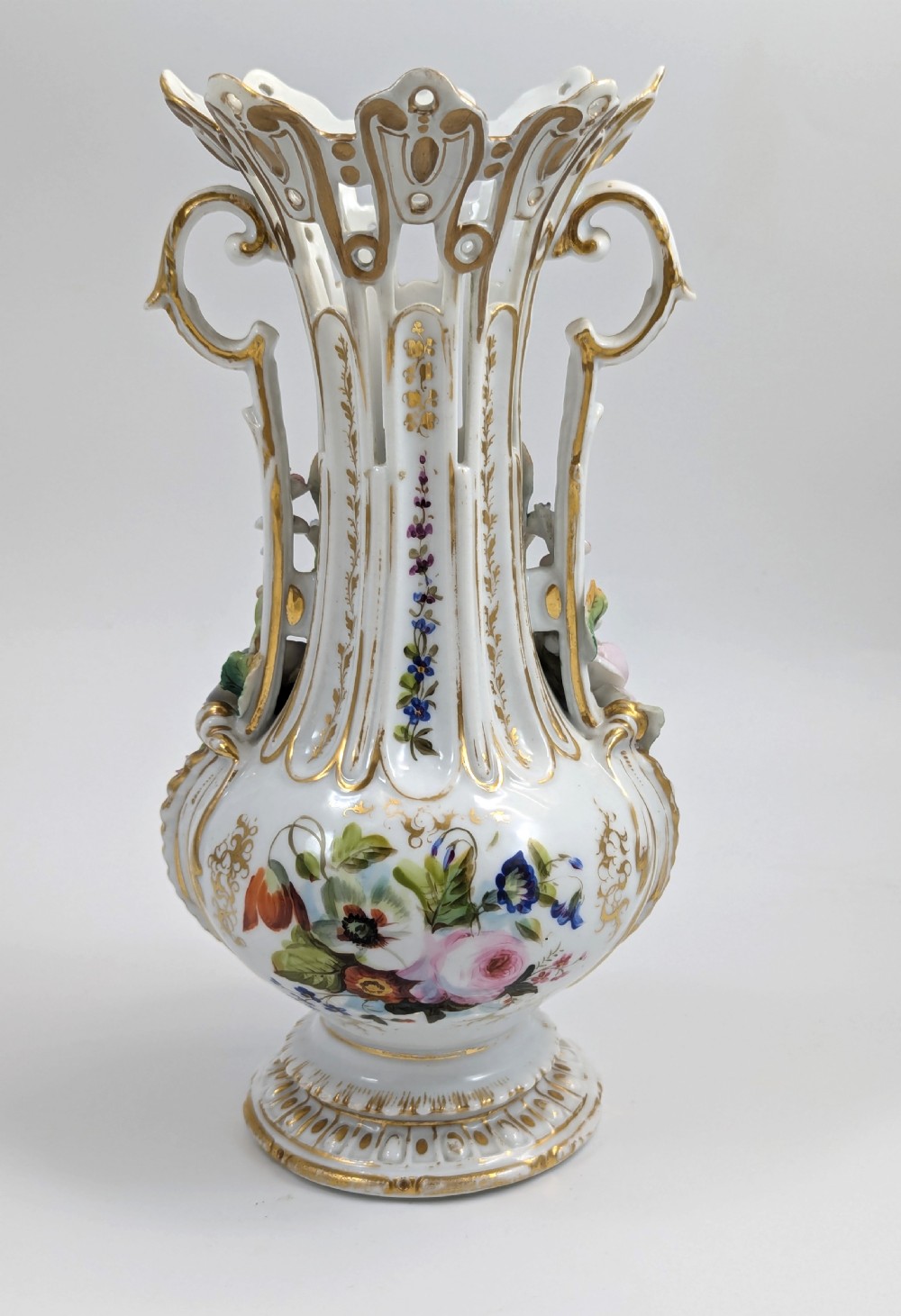 A pair of nineteenth-century white hard-paste porcelain vases featuring reticulated necks, gilded scroll handles, painted botanical panels, and applied ceramic flowers. View VI