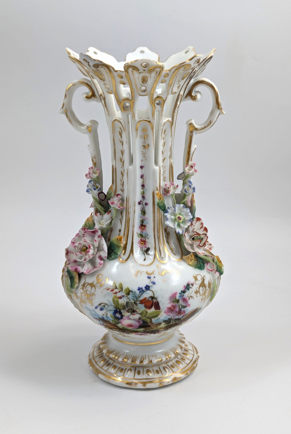 A pair of nineteenth-century white hard-paste porcelain vases featuring reticulated necks, gilded scroll handles, painted botanical panels, and applied ceramic flowers. View VII