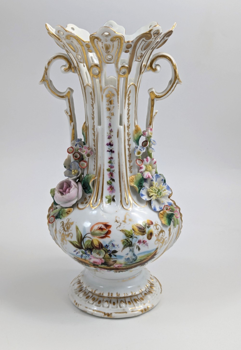 A pair of nineteenth-century white hard-paste porcelain vases featuring reticulated necks, gilded scroll handles, painted botanical panels, and applied ceramic flowers. View XII
