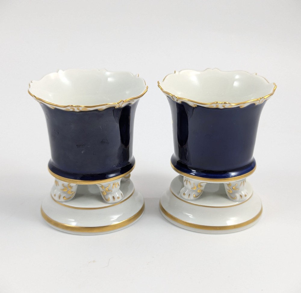 A pair of small Meissen cobalt blue porcelain vases featuring scalloped gilt rims, hand-painted floral cartouches, scroll feet, and circular white bases. View III