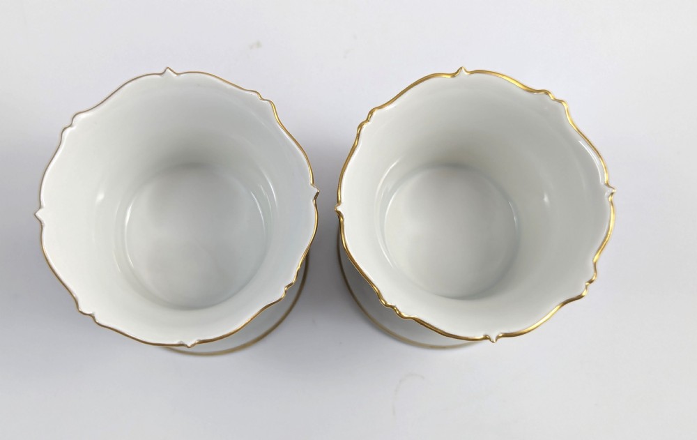 A pair of small Meissen cobalt blue porcelain vases featuring scalloped gilt rims, hand-painted floral cartouches, scroll feet, and circular white bases. View VII