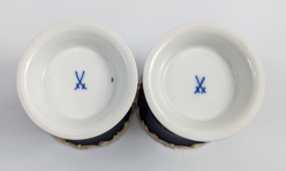 A pair of small Meissen cobalt blue porcelain vases featuring scalloped gilt rims, hand-painted floral cartouches, scroll feet, and circular white bases. View IX