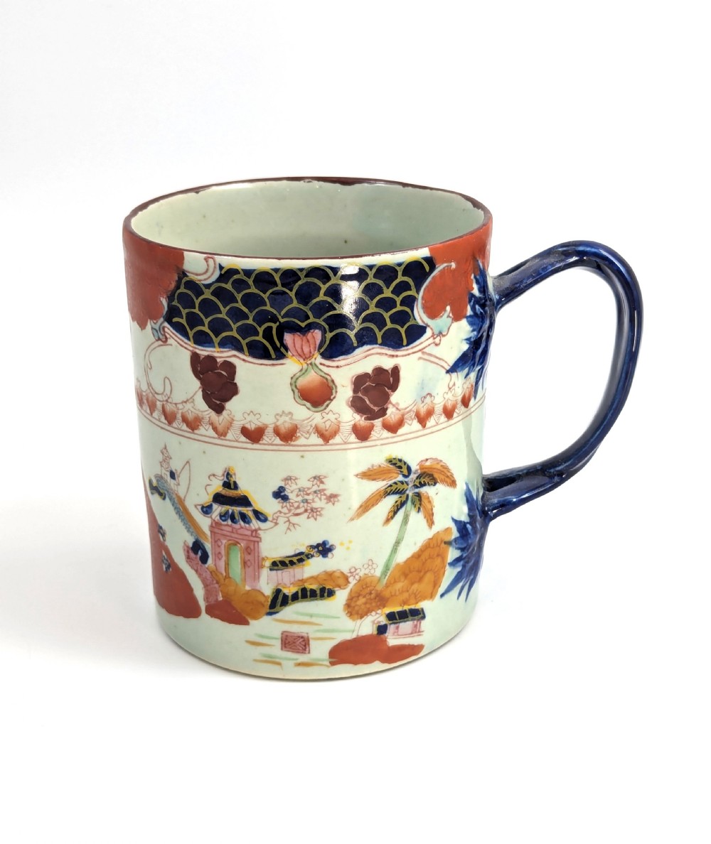 A cylindrical antique Chinese Kangxi porcelain tankard decorated with hand-painted pagodas, palm trees, and an iron-red scale pattern border.