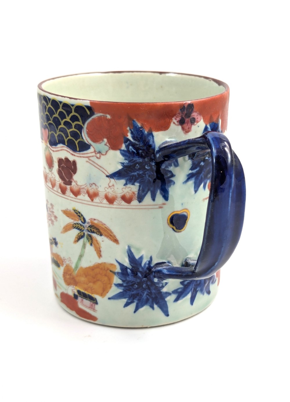 A cylindrical antique Chinese Kangxi porcelain tankard decorated with hand-painted pagodas, palm trees, and an iron-red scale pattern border. View II