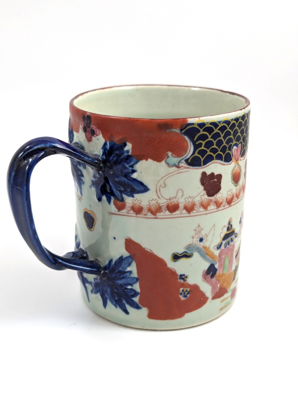 A cylindrical antique Chinese Kangxi porcelain tankard decorated with hand-painted pagodas, palm trees, and an iron-red scale pattern border. View III