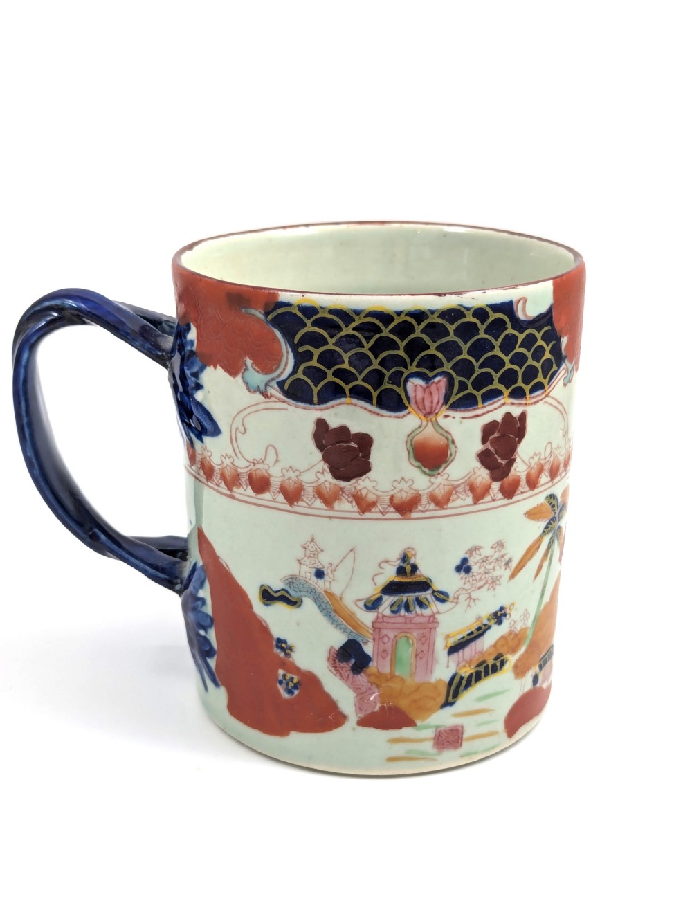 A cylindrical antique Chinese Kangxi porcelain tankard decorated with hand-painted pagodas, palm trees, and an iron-red scale pattern border. View IV