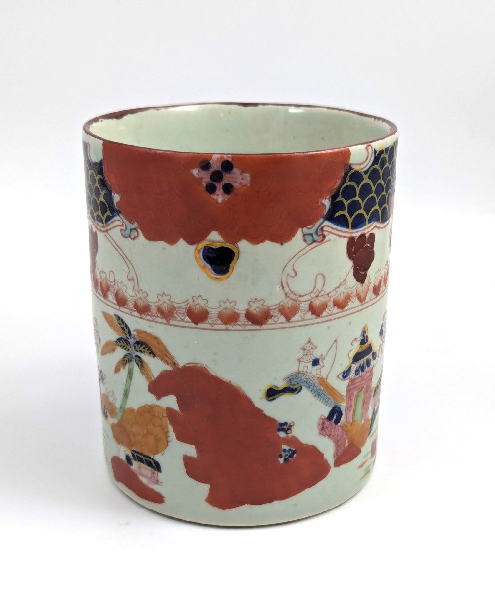 A cylindrical antique Chinese Kangxi porcelain tankard decorated with hand-painted pagodas, palm trees, and an iron-red scale pattern border. View VI