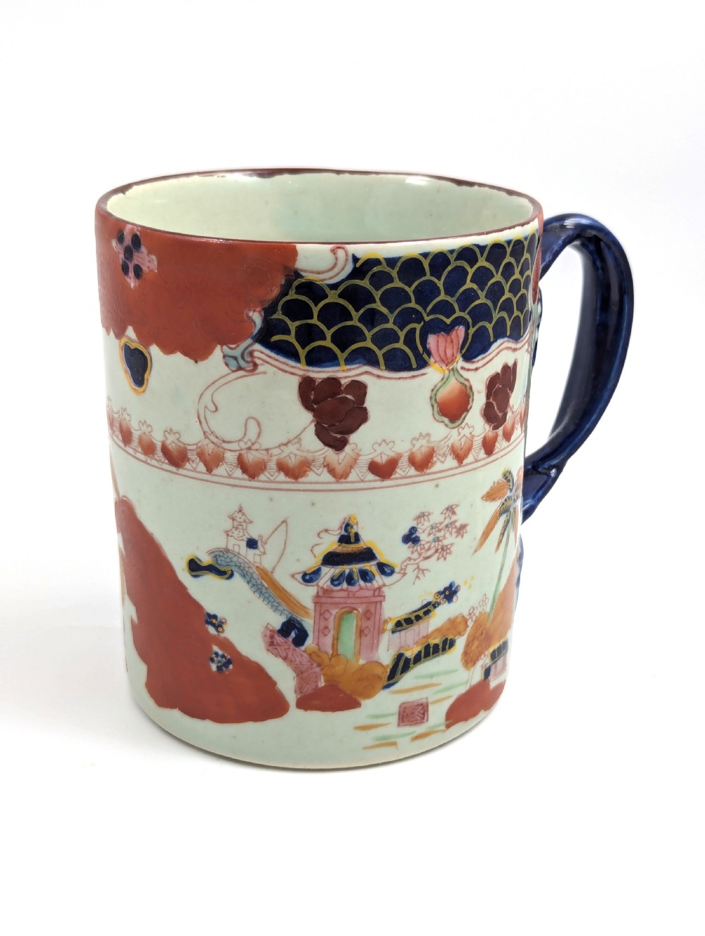 A cylindrical antique Chinese Kangxi porcelain tankard decorated with hand-painted pagodas, palm trees, and an iron-red scale pattern border. View VII