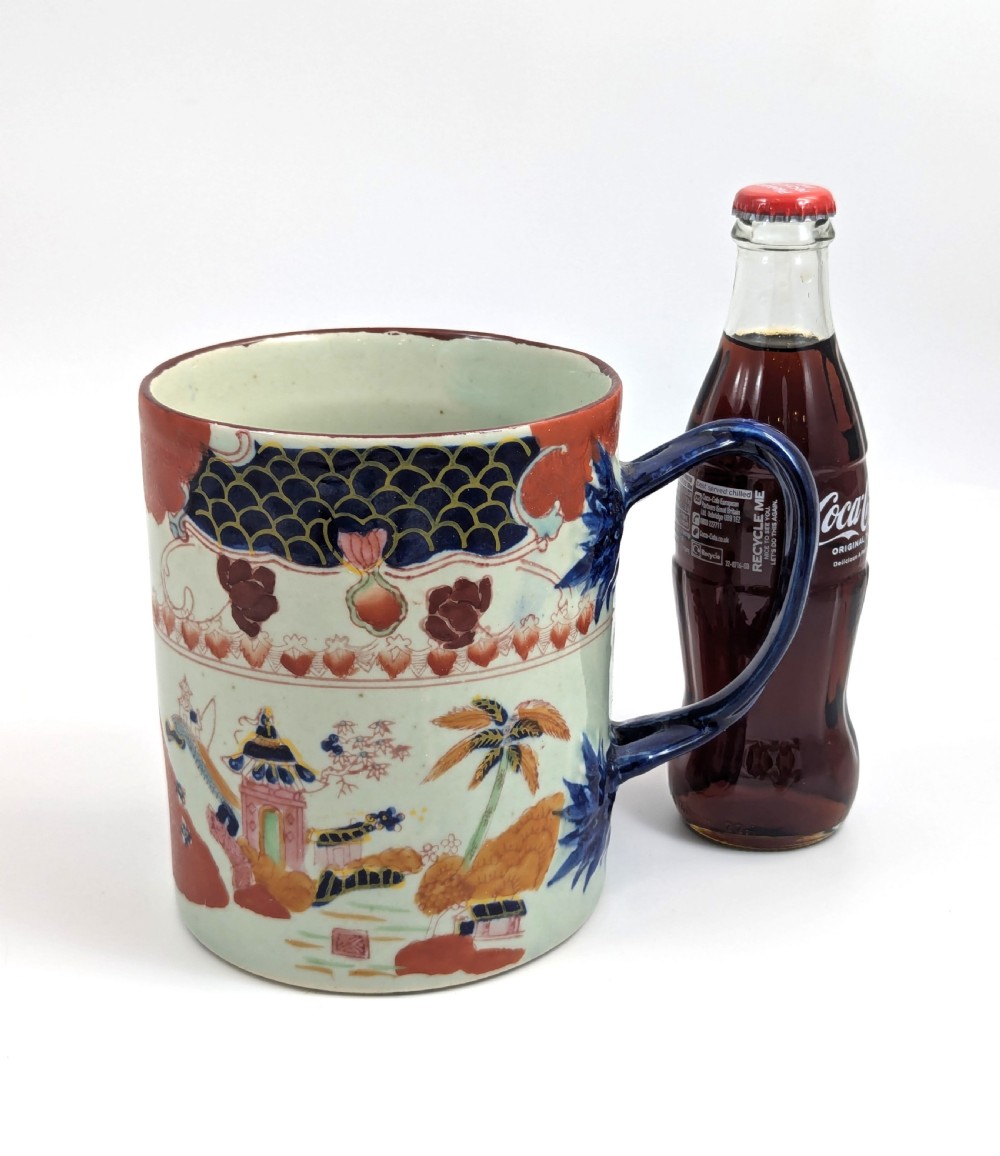 A cylindrical antique Chinese Kangxi porcelain tankard decorated with hand-painted pagodas, palm trees, and an iron-red scale pattern border. View X
