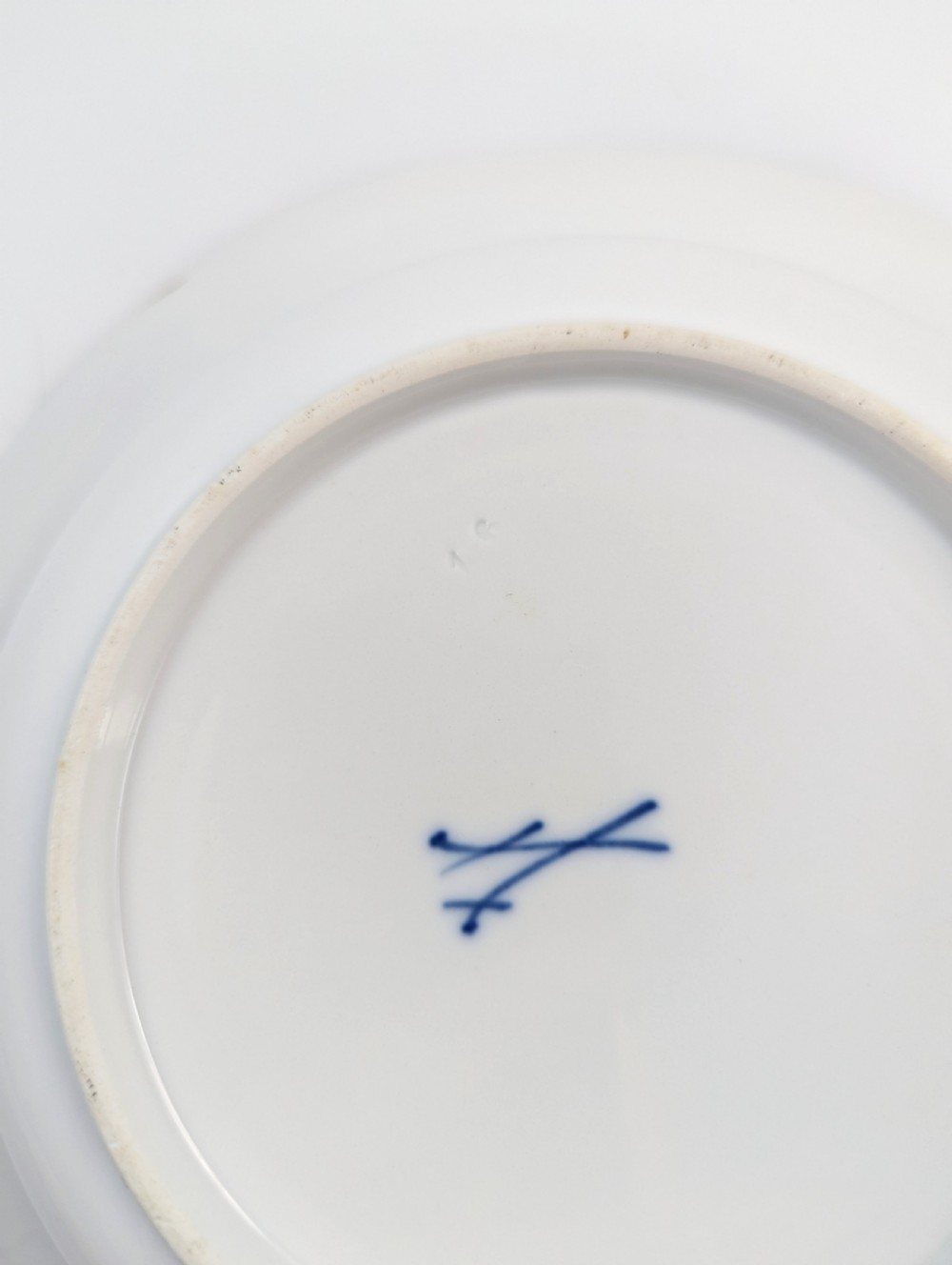An antique white hard-paste porcelain plate decorated with hand-painted Kakiemon style motifs of a yellow tiger, purple bird, and flowering branches with a scalloped dark rim. View V