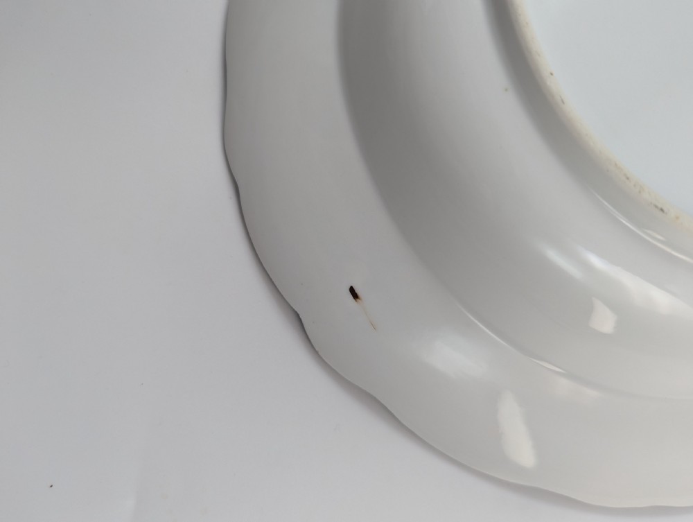 An antique white hard-paste porcelain plate decorated with hand-painted Kakiemon style motifs of a yellow tiger, purple bird, and flowering branches with a scalloped dark rim. View VI
