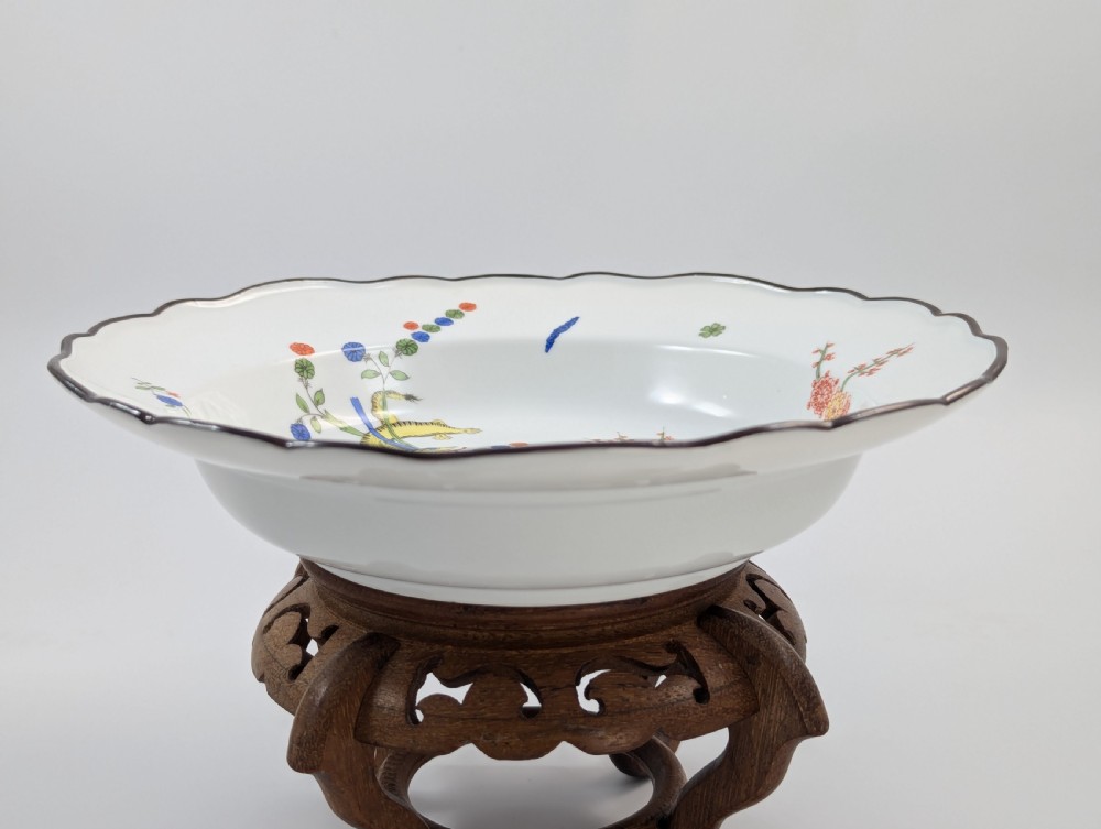 An antique white hard-paste porcelain plate decorated with hand-painted Kakiemon style motifs of a yellow tiger, purple bird, and flowering branches with a scalloped dark rim. View VII