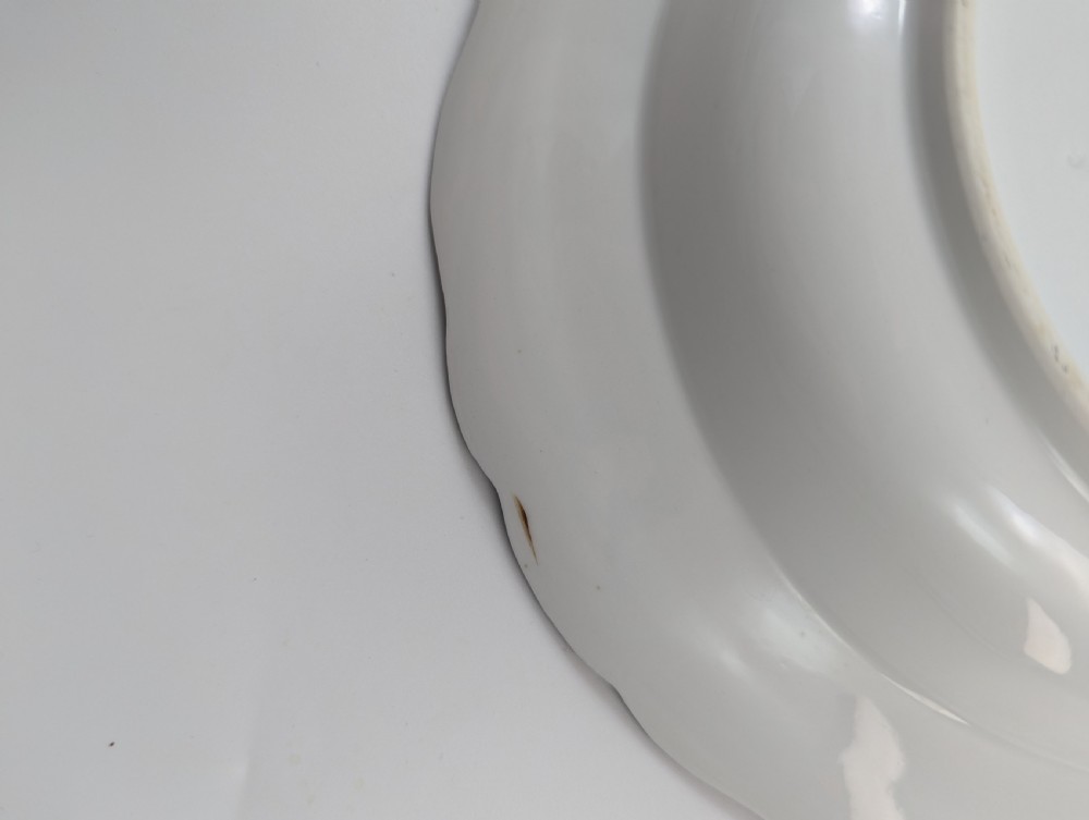 An antique white hard-paste porcelain plate decorated with hand-painted Kakiemon style motifs of a yellow tiger, purple bird, and flowering branches with a scalloped dark rim. View VIII