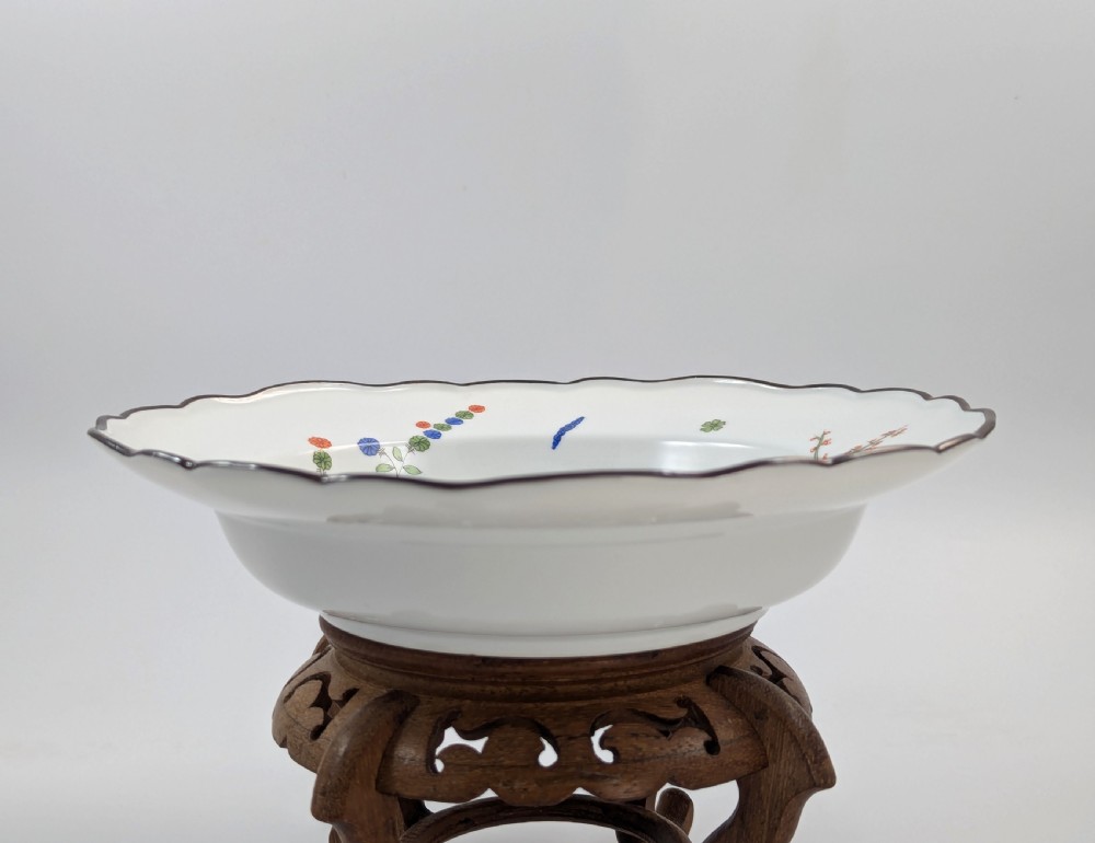 An antique white hard-paste porcelain plate decorated with hand-painted Kakiemon style motifs of a yellow tiger, purple bird, and flowering branches with a scalloped dark rim. View IX
