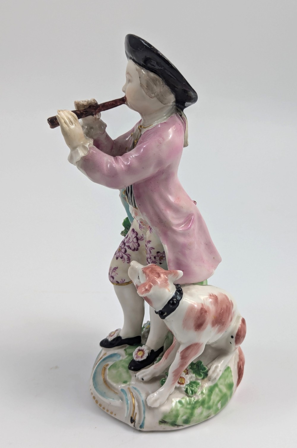 An 18th-century Derby soft-paste porcelain figurine depicting a shepherd playing a pipe with a dog standing beside him on a gilded scroll base. View III
