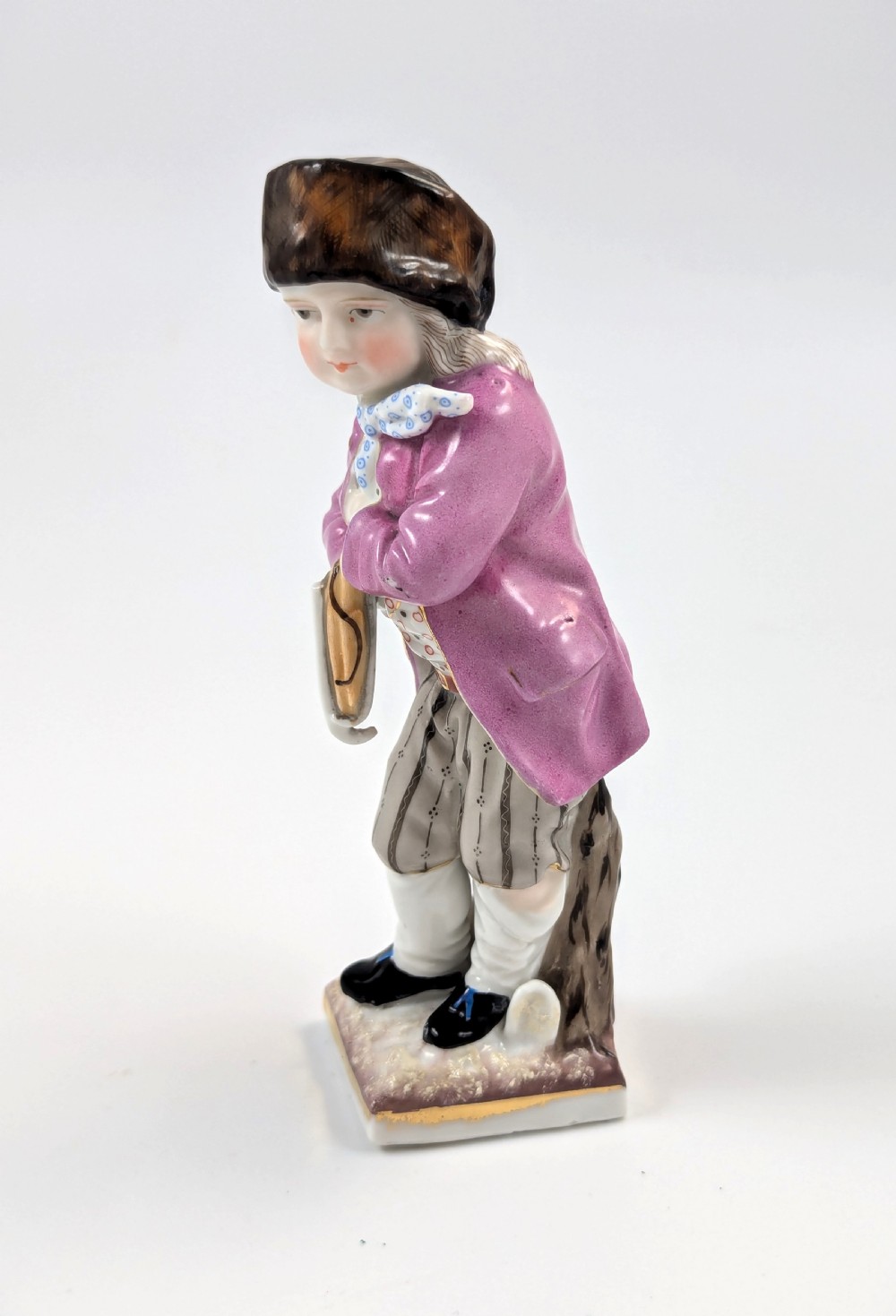 A hand-painted 19th-century Sitzendorf porcelain figurine depicting a male ice skater wearing a pink coat, patterned scarf, and fur-trimmed hat. View II
