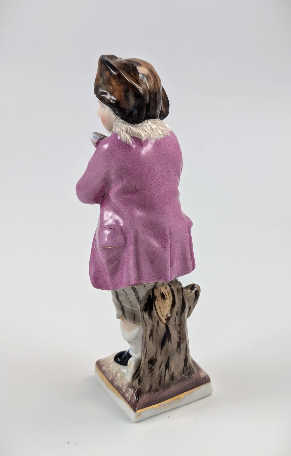 A hand-painted 19th-century Sitzendorf porcelain figurine depicting a male ice skater wearing a pink coat, patterned scarf, and fur-trimmed hat. View III