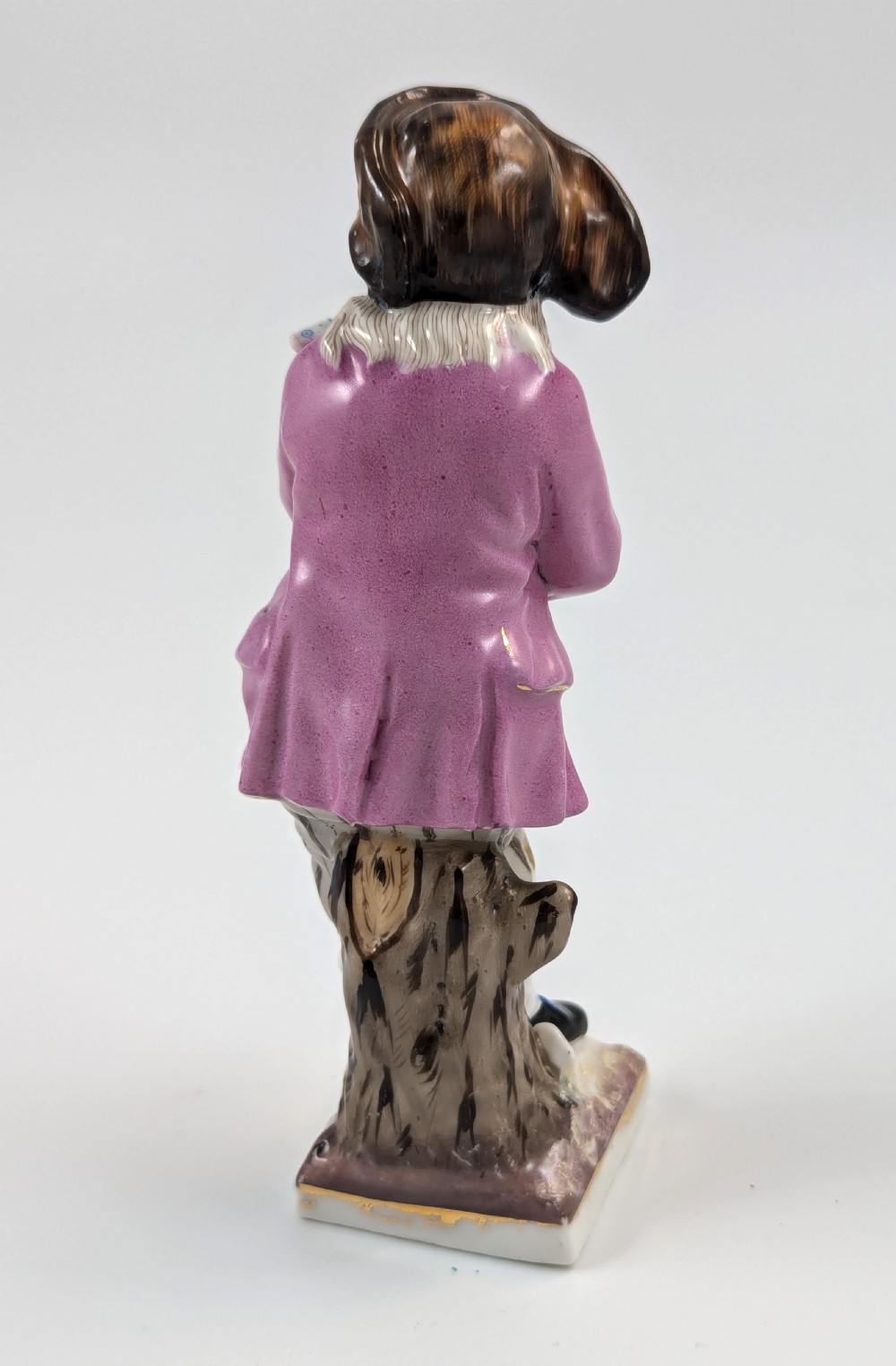 A hand-painted 19th-century Sitzendorf porcelain figurine depicting a male ice skater wearing a pink coat, patterned scarf, and fur-trimmed hat. View IV