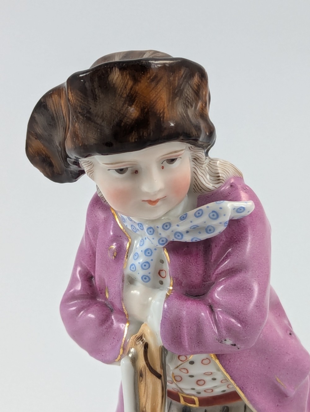 A hand-painted 19th-century Sitzendorf porcelain figurine depicting a male ice skater wearing a pink coat, patterned scarf, and fur-trimmed hat. View VIII