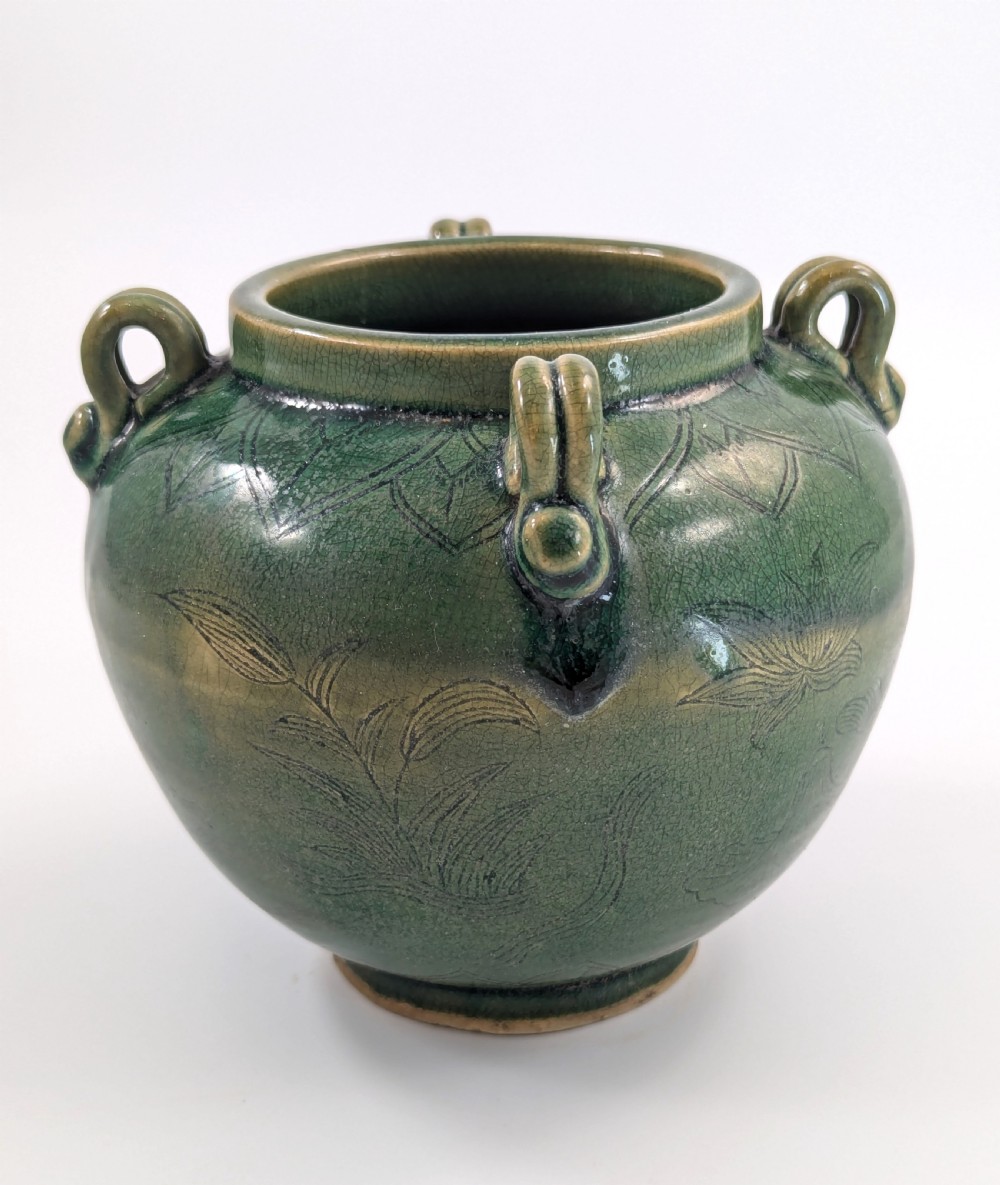 A rounded olive green celadon ceramic jar with four loop handles along the rim, featuring crackle glaze and incised line drawings of ducks and lotus plants. View IV