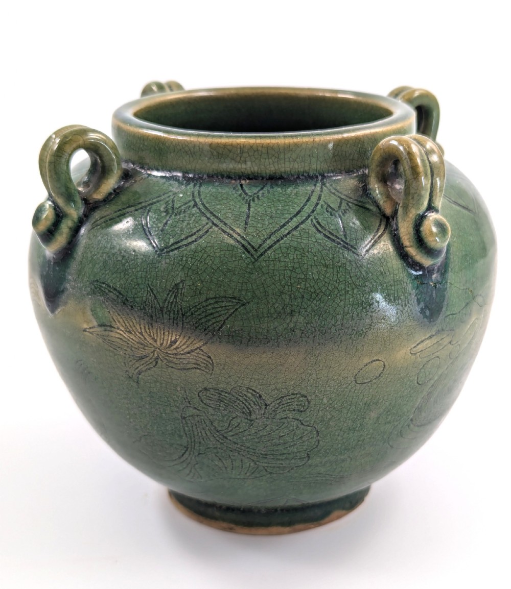 A rounded olive green celadon ceramic jar with four loop handles along the rim, featuring crackle glaze and incised line drawings of ducks and lotus plants. View V