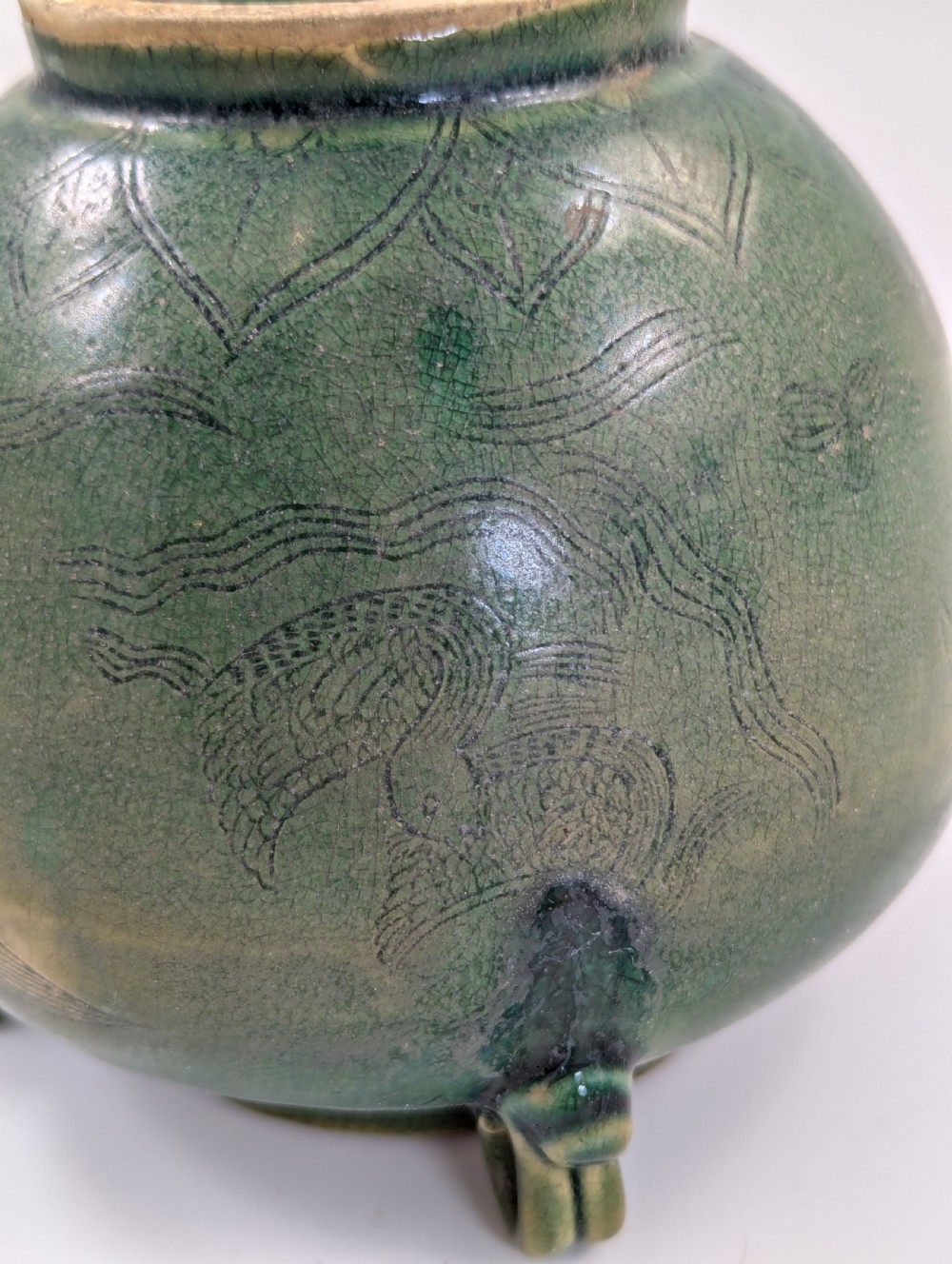 A rounded olive green celadon ceramic jar with four loop handles along the rim, featuring crackle glaze and incised line drawings of ducks and lotus plants. View VIII
